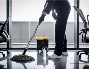 Pessoa limpando o piso de um escritório com um esfregão, enfatizando a importância da limpeza para um ambiente de trabalho saudável.